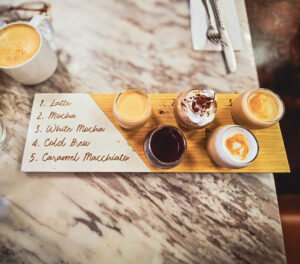 offee flight with four small glasses of cold brew, caramel macchiato, latte, and seasonal specialty coffee on a wooden board at JoJo Coffeehouse in Scottsdale.