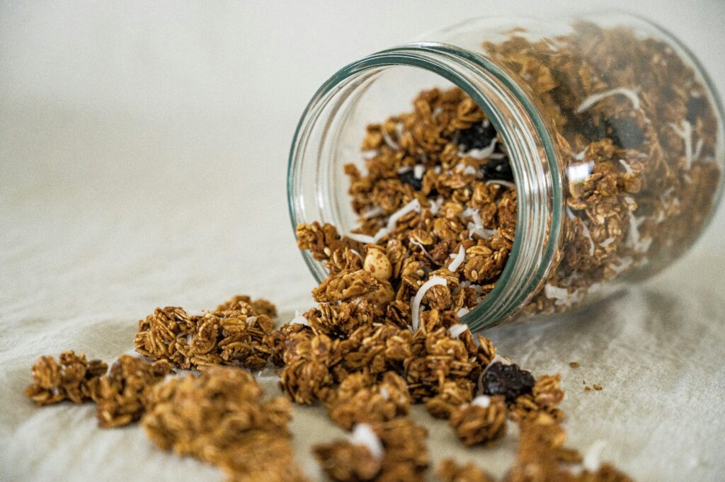 Homemade granola clusters spilling from a glass storage jar