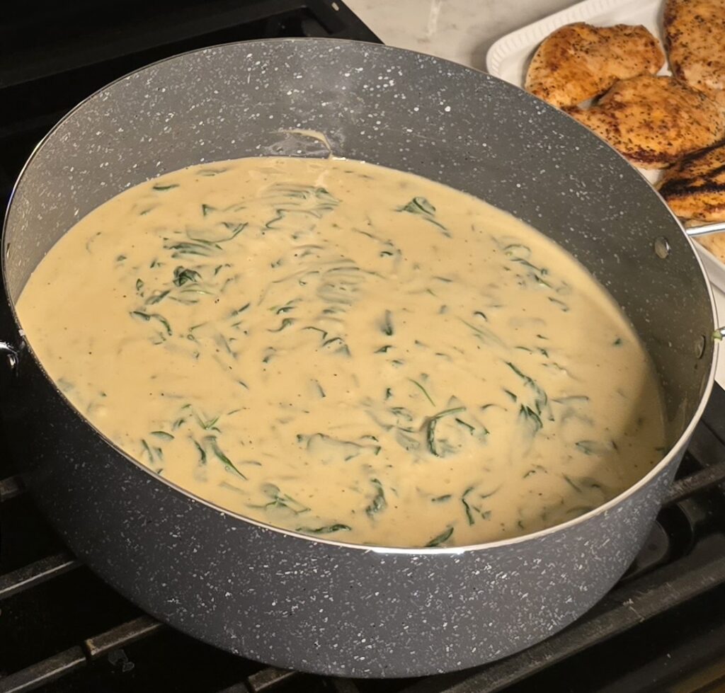 Creamy lemon garlic Parmesan sauce with wilted spinach simmering in a large skillet.