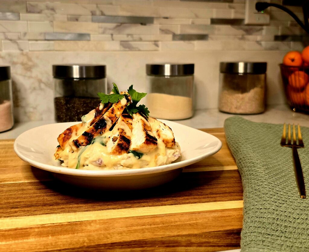 Plated lemon garlic Parmesan chicken served over mashed potatoes, topped with creamy spinach sauce and fresh herbs.
