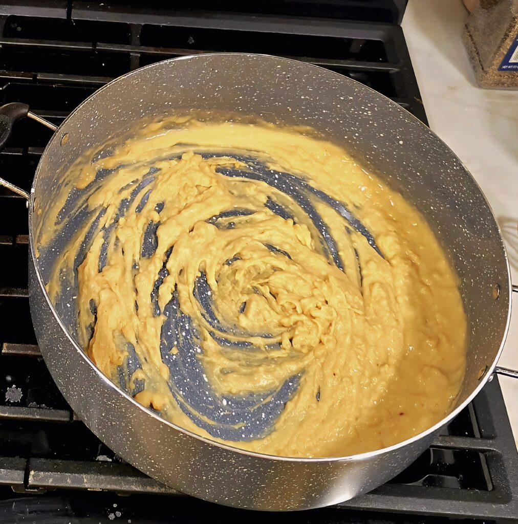 Creamy lemon garlic Parmesan sauce thickening in a skillet as the roux and stock are whisked together.