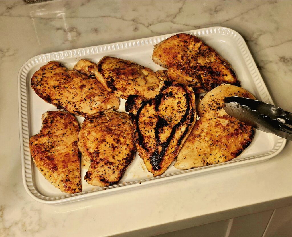 Golden-seared chicken breasts resting on a tray after being cooked in a skillet.