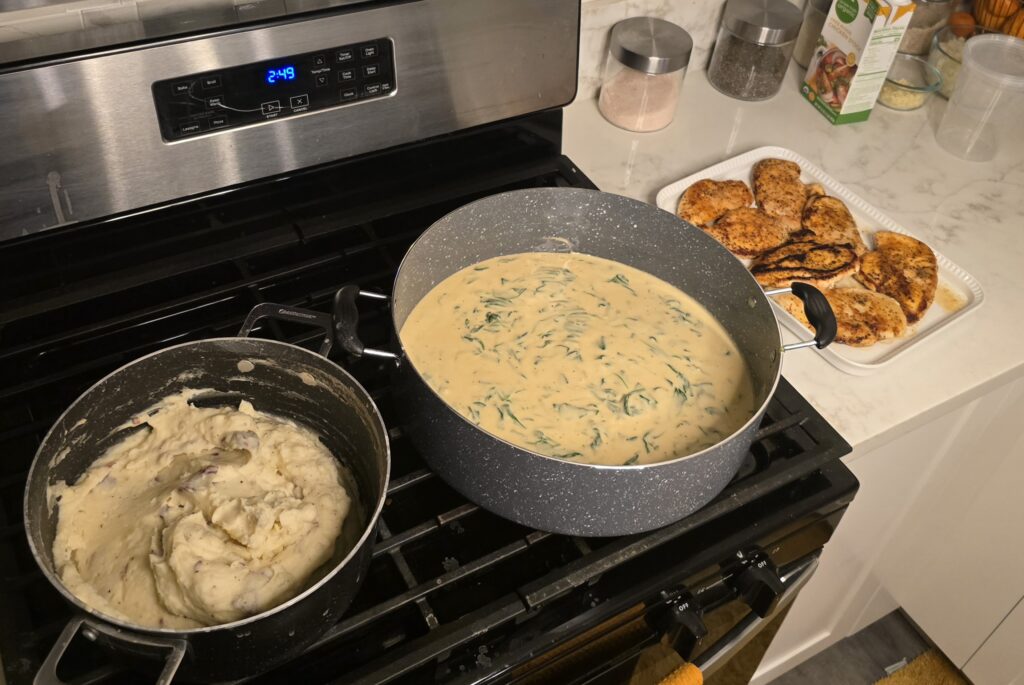 Creamy lemon garlic Parmesan sauce with spinach simmering on the stove while seared chicken rests on a tray nearby.